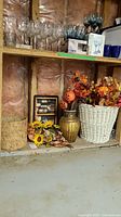 Overall view of the items in the set including the white basket filled with faux fall foliage and pumpkin stakes, smaller natural basket, decorative urn and placemat.