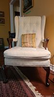 Front view of ivory wing back chair with button tufting and small striped accent pillow
