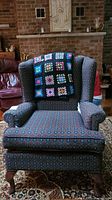 Front view of wing back chair with patterned upholstery and granny square afghan draped over backrest.