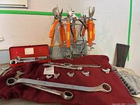 Photo showing orange-handled pliers on rack, combination wrenches on fabric holder, large wrenches, and socket wrench in red case
