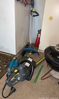 Photo showing Yardworks battery-powered leaf blower, hedge trimmer, and weed wacker together on the floor near a wall and fire extinguisher.