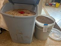 Grey trash can and white pail, both filled with dry absorbent