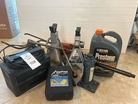 Group shot of all automotive accessories: two jack stands, two bottle jacks, charger, coolant jug, wheel chocks case