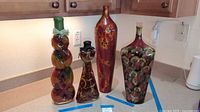 All four decorative bottles and vases displayed on countertop with height tape for scale