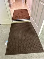 Wide view showing both mats in doorway, larger grid mat outside, smaller diamond mat inside