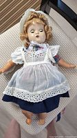 Full view of doll with dress, pinafore and bonnet