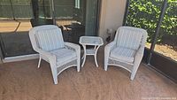 Two white wicker armchairs with cushions and matching side table