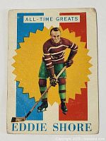 Front side of the vintage 1960-61 Topps Eddie Shore hockey card showing the player in striped hockey jersey and green pants on a colorful background.