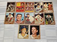 Photo overview of 13 assorted 1962 Topps baseball cards laid out on a flat surface showing front face of each card, featuring mostly pitcher and batter poses with mixed graphical card fronts and backgrounds in color.