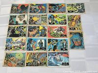 Top view of a collection of 20 vintage 1966 Topps Batman trading cards laid out on a white surface showing various comic-book style scenes and characters.
