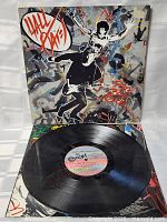 Photo of vinyl record partially out of its cover showing multi-colored center label with album details and black vinyl surface.