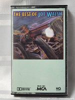 Front cover of 'The Best of Joe Walsh' cassette tape showing artwork of a vintage car headlight and engine.