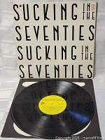 Vinyl record disc with yellow label showing album and artist details, placed partially out of sleeve.