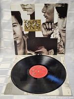 Vinyl disc placed on top of album cover, showing orange label and glossy black vinyl surface.