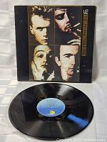 Vinyl record with blue label lying in front of album cover, showing surface condition.