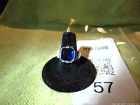 Front view of a sterling silver ring with a prominent square-cut blue cubic zirconia gemstone set in the center, displayed on a black ring holder.