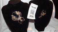 Both brooches displayed on black stands showing size and details