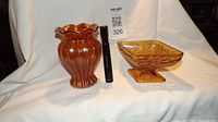 Two amber carnival glass pieces: a vase with ruffled top and a square candy dish on a pedestal base with floral patterns.