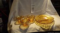 Three amber carnival glass cups and one divided dish with matching leaf and grape pattern displayed on white fabric background