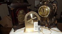 Three mantle clocks displayed on a white surface, showing details of design, condition and relative sizes