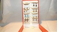 Full frontal view of the seven pairs of earrings on a white display with orange trim, showing piercing types and general styles.