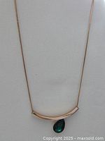 Full view of costume necklace with gold-tone curved bar and teardrop green stone pendant on thin chain.
