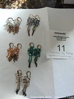 Five pairs of handmade vintage costume earrings laid out on white paper, showing different designs with metal leaf charms and beads.