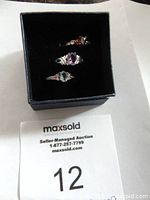 Three costume rings displayed inside a black presentation box with visible stones and silver tone bands.