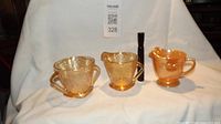 Three cream and sugar pieces: one solid orange Fire King creamer, two clear orange depression glass cream and sugar with floral etching