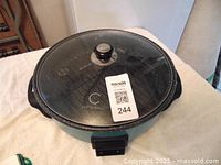 Top view of Curtis Stone round indoor electric grill showing glass lid with black handle and logo visible beneath lid.