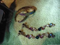 Long dangling earrings with multiple colored CZ stones and colorful hoop earrings on green textured surface.