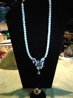 Full view of the pearl necklace on a display bust with attached watch ring showing overall length and wear condition.