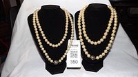Two black necklace display stands showing two strands of faux pearl necklaces with rhinestone magnetic clasps side by side.