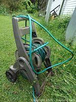 Side angle view of beige plastic garden hose reel with green hose wrapped and placed on grass outdoors with some dirt and debris on it.