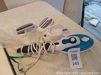 Photo of the handheld clothes steamer with power cord, multiple attachments including brushes, measuring cup, and stand placed on a beige surface.