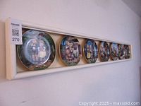 Seven Hummel decorative plates mounted in a white homemade wooden display case.