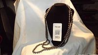 Photo showing the Joan Rivers faux grey pearl necklace draped over a black jewelry bust with a white cloth background. The necklace beads are shiny grey faux pearls.
