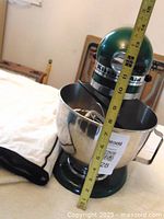 Green KitchenAid Classic stand mixer with measuring tape showing size and fabric cover beside it.