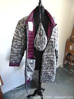 Full view of the light multi-use coat on a black mannequin, showing pattern, maroon lining, and attached carry bag.