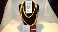 Three yellow pearl necklaces displayed on a black stand showing graduated bead sizes and gloss finish.