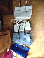 Four purses arranged on the floor showing different colors, materials and styles.