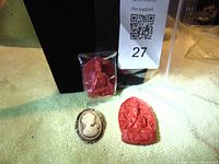 Lot showing one cameo pin and two red religious pendants against a black background.