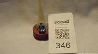 Front view of gold plated ring with blue oval stone on a display stand alongside a MaxSold card labeled 346.