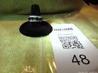 Front view of ring on black velvet holder showing green gemstones and surrounding cubic zirconia stones