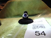 Front view of sterling silver ring with blue oval CZ surrounded by clear CZ stones on black velvet stand against a yellow background.