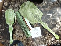 Top view of the green hairbrush, two combs, and hand mirror on marble surface with a lot number card