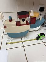 Two hand carved and painted decorative nautical boats on a tiled surface with a measuring tape showing length