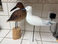 Close-up photo showing the two seagulls on their respective stands placed on a white tiled countertop.