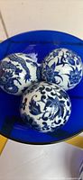 Three vintage blue and white porcelain carpet balls inside a blue bowl showing detailed designs