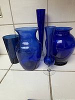 All five cobalt blue glass vases shown together, arranged on tiled surface.